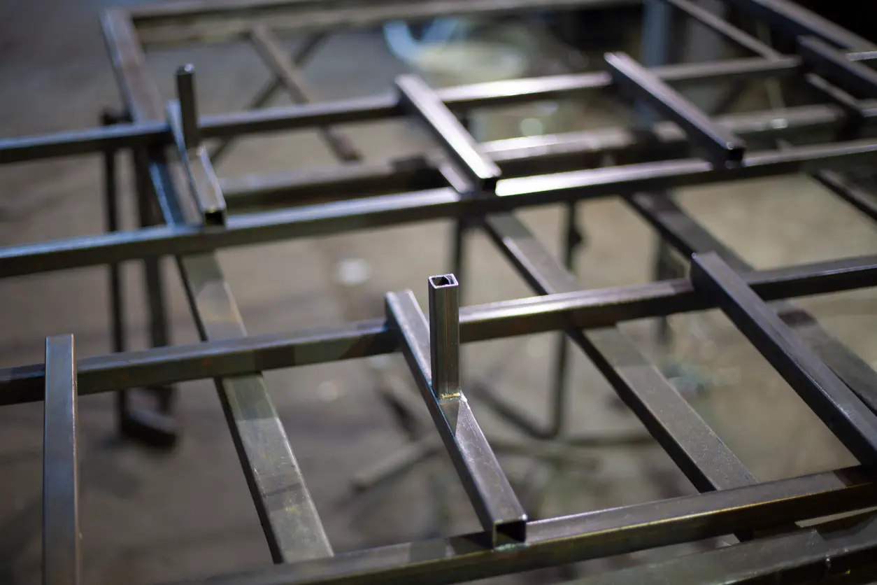 Vue rapprochée des cadres de meubles en tube d'acier soudé dans un atelier de fabrication métallique, avec les poteaux rigides en attente de montage.